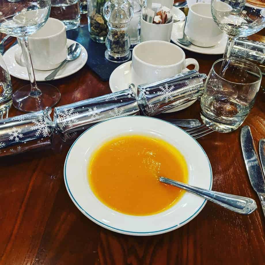 Bowl of soup on wooden table with Christmas decor, cups and glasses