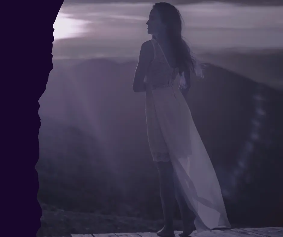 Silhouette of a woman in a white dress standing confidently on a mountain peak at sunset, symbolizing personal power and standing tall.