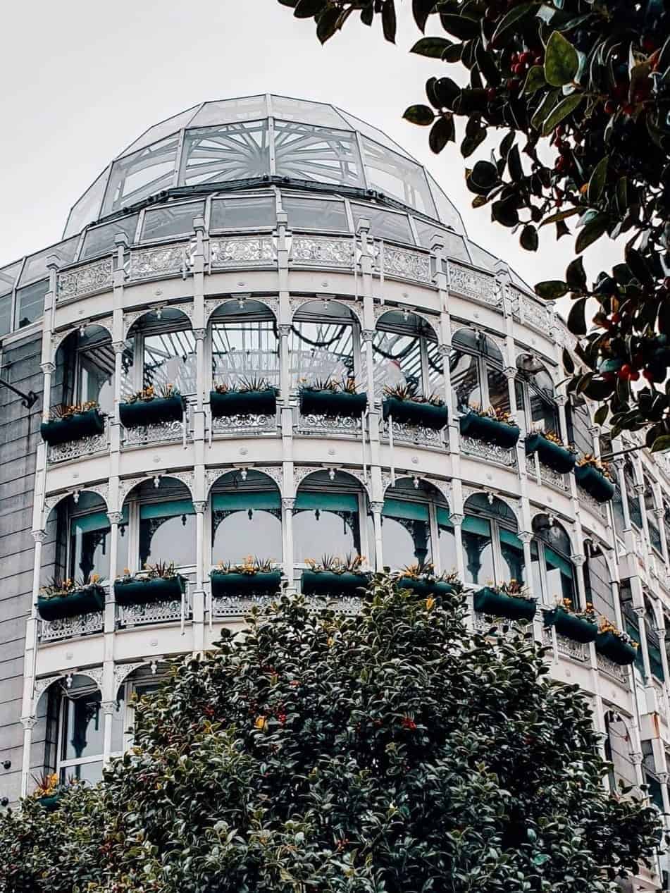 The St Stephen's Green Shopping Centre in Dublin, featuring its ornate Victorian-style facade with multiple arches and potted plants, viewed from street level.