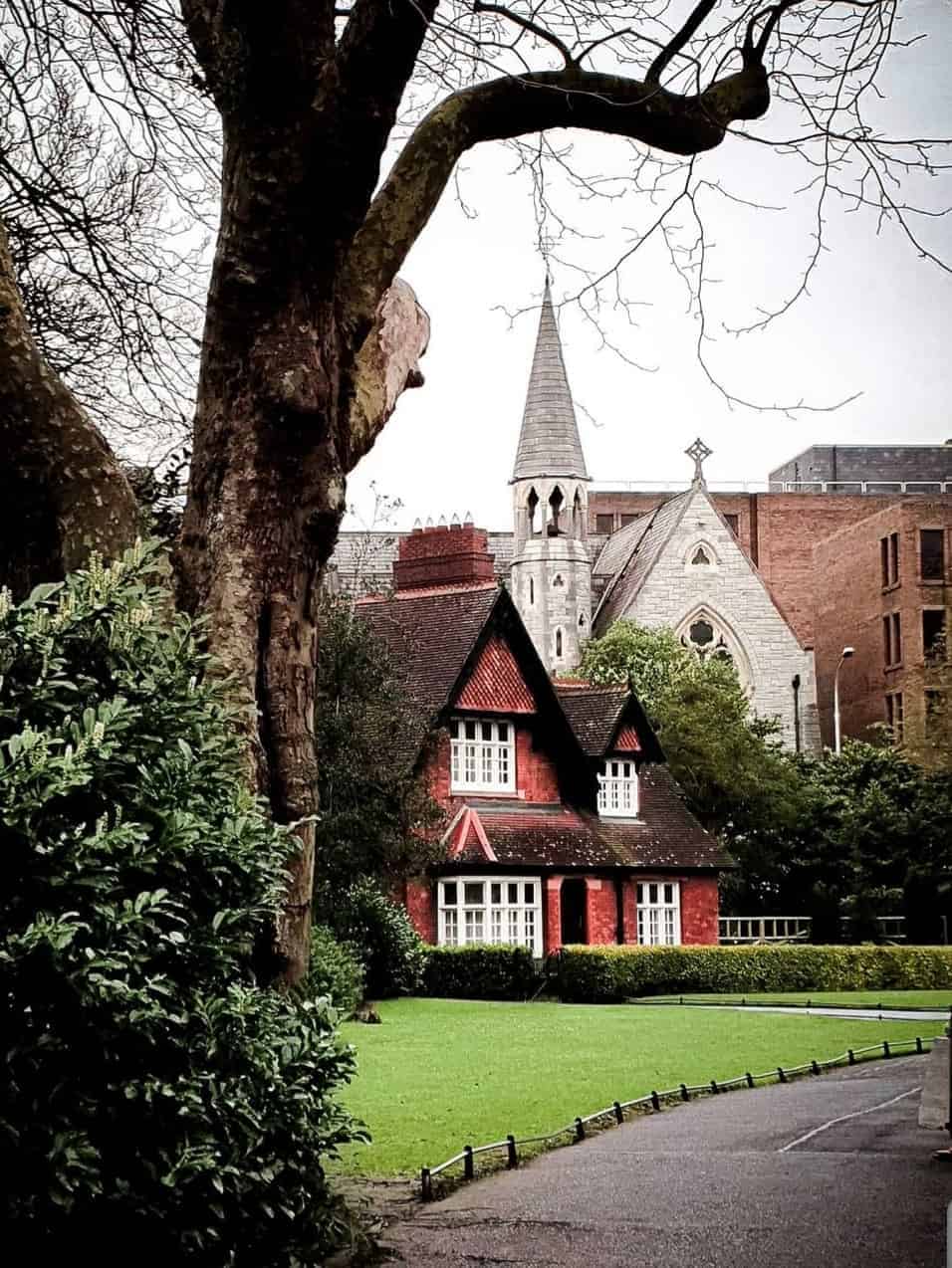 A charming Victorian house with red brick and pointed roof, located in St Stephen's Green Park, Dublin, framed by trees and greenery.