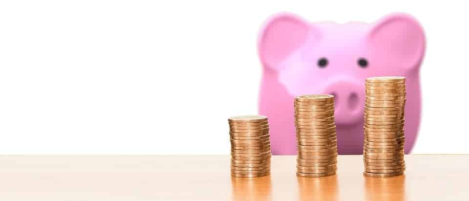 Stacks of coins on a wooden surface with pink piggy bank in background