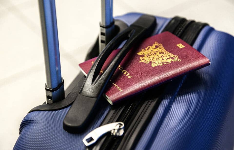 A blue suitcase with a black zip that has a red passport sitting on the top.