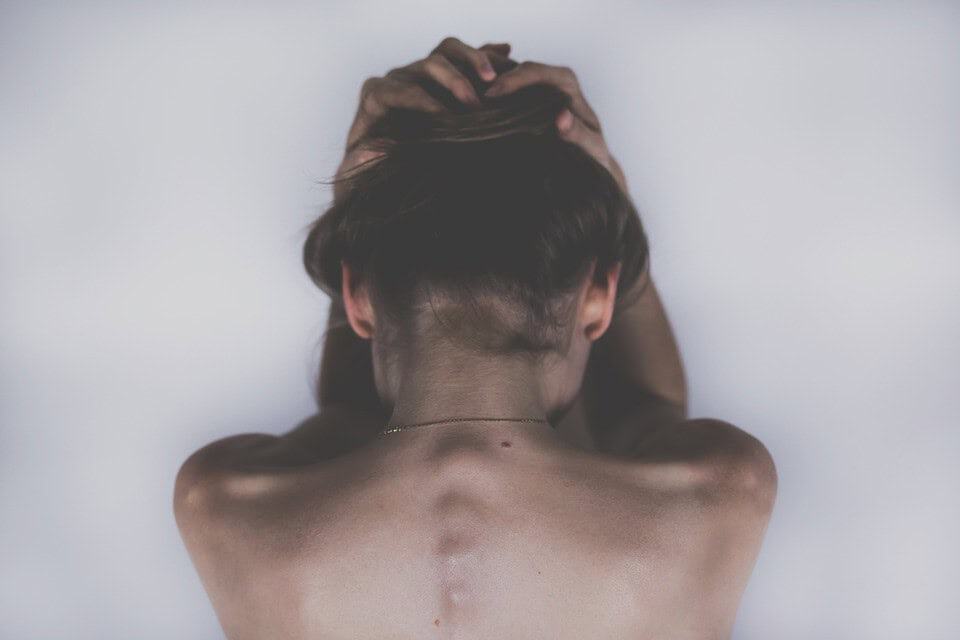 A person with their head in their hands leaning against a white wall