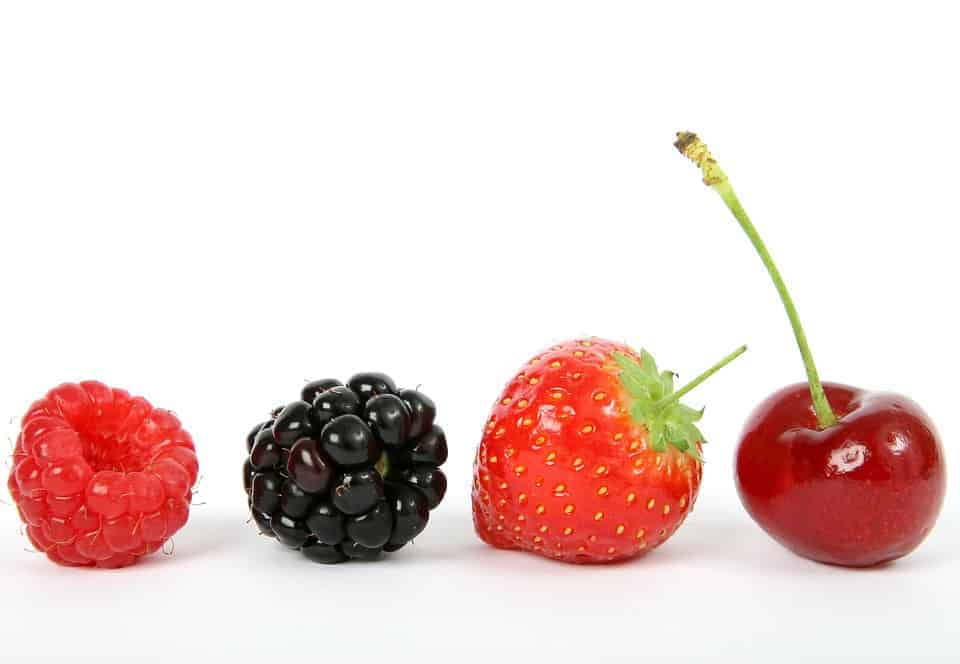 a raspberry, a blackberry, a strawberry and a cherry all placed on a white surface