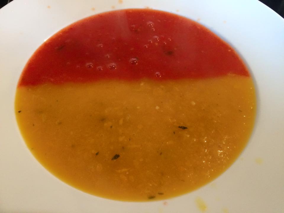 A soup made with red and yellow peppers, the bowl is filled with half red soup and half yellow soup
