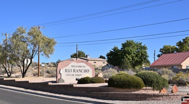 A roadside sign welcoming visitors to Rio Rancho, New Mexico, featuring the city's tagline 'City of Vision' and a backdrop of residential homes.