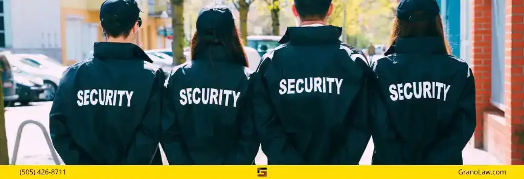 Four security guards seen from the back, standing in a line. They are wearing dark blue jackets with "SECURITY" printed in white across the back. The image footer has a yellow bar with "(505) 426-8711" on the left, a logo in the center, and "GranoLaw.com" on the right.