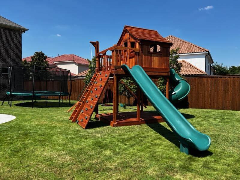 BFF playset A vibrant Backyard Fun Factory playset situated in a spacious, scenic backyard, featuring engaging attachments such as a rocket and spiral slide, climbing wall, and an upper covered deck, all designed to inspire fun and creativity.