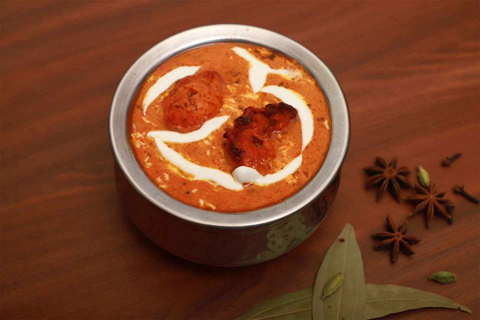 Savory Indian chicken curry served in a traditional stainless steel bowl, garnished with cream swirls, highlighting delicious flavors perfect for biryani and Indian cuisine lovers.