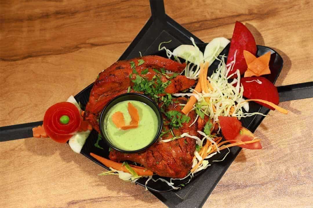 Grilled fish served with fresh vegetables and mint chutney in a black dish, highlighting flavorful Indian cuisine at Biryani Place.