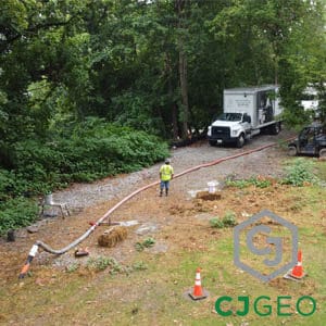 A CJGeo crew member pumping flowable fill or grout through a long hose at a remote project site.
