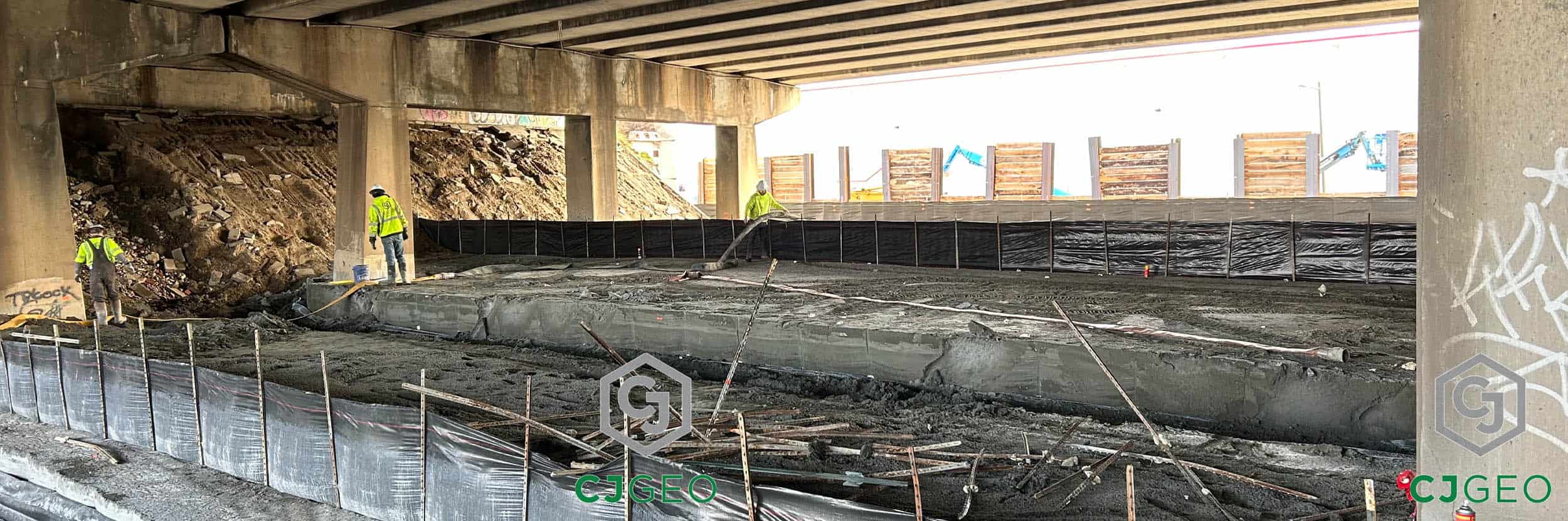 A CJGeo crew placing and finishing a large volume of lightweight cellular concrete as fill material under a bridge overpass.