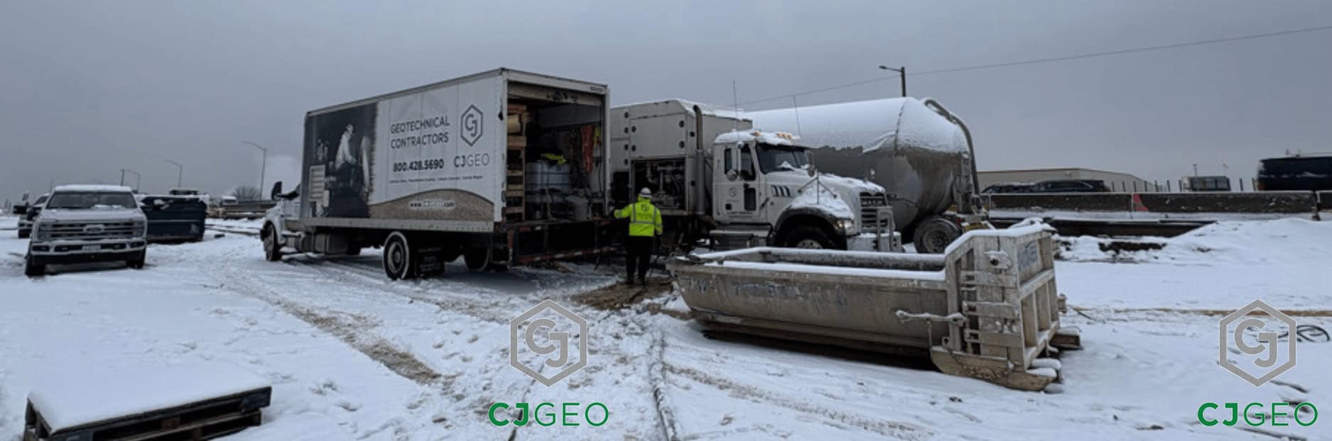 A dry batch cellular concrete plant, a cement pig, and a support vehicle from CJGeo are set up on a snow-covered job site under an overcast sky.