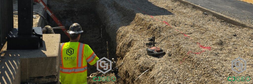 A CJGeo worker wearing a high visibility vest performing polyurethane compaction grouting in a trench.