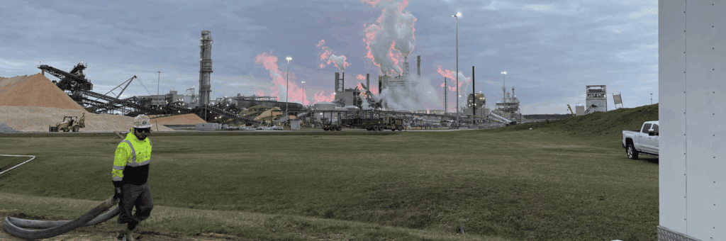A CJGeo worker pulling a rose through a field with a paper mill in the background during sunset.