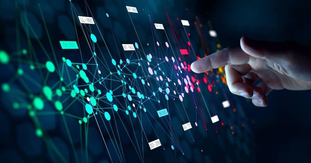 Um dedo humano interage com uma rede digital complexa de pontos coloridos e linhas em um fundo escuro, exibindo rótulos de dados.