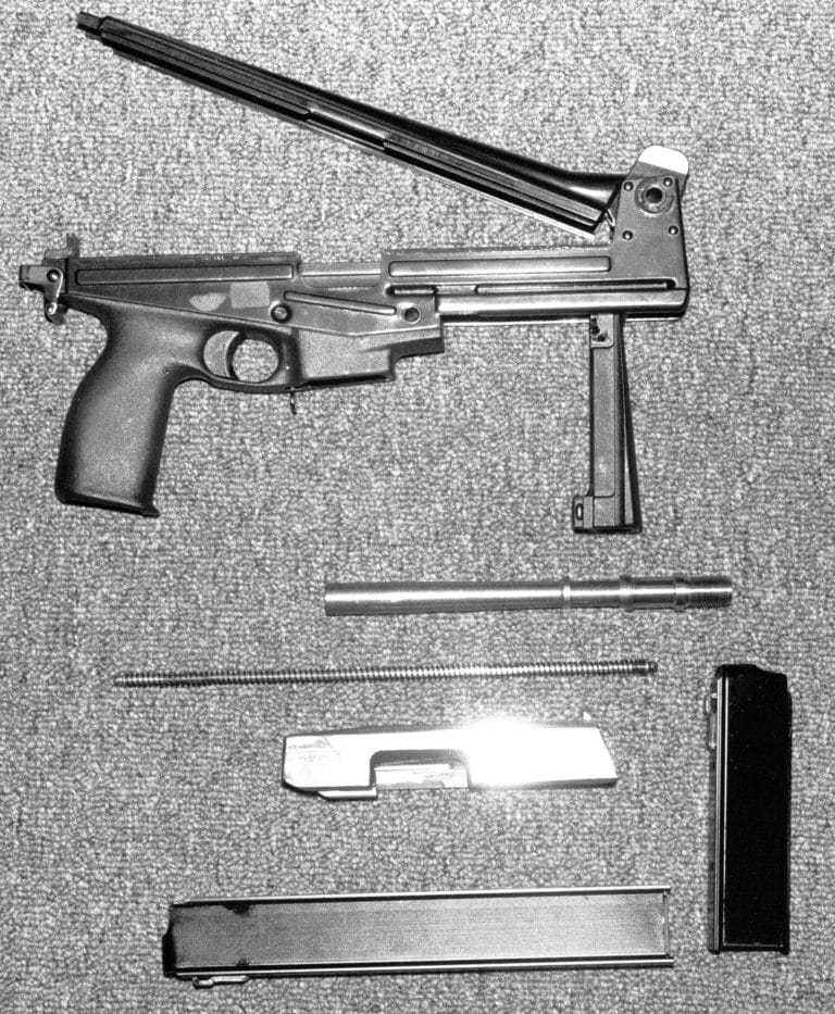 The field stripped Jati-Matic with the top of the receiver open. One of the weaknesses of the design can be seen in this picture. The receiver cover release is at the rear of the receiver body. It is pulled down to release the cover. Part of the cover release is also the rear sling swivel. If the sling is pulled down, the top of the receiver can be inadvertently released by the operator. PHOTO CREDIT: Kevin Dockery