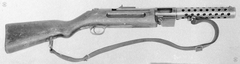 A lower right side view of the modified MP18-I submachinegun. The bolt and mainspring are missing on this specimen. On the left side of the new magazine housing is a straight magazine well to take a 20-round double column magazine. Because of the modification of the magazine housing from the single column snail drum magazine to the straight box double column design, the rounds had to be presented to the chamber from a single position for proper feeding. This was the weakest point in the weapons design at it continued to be used in German and other countries for decades. The hinge for opening the weapon is plain in this view underneath and part of the magazine housing. PHOTO CREDIT: US Army