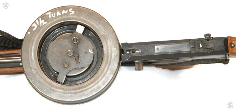 An upper close-up view of the top of the receiver and drum. Just behind the drum on the top of the receiver is the serrated magazine release. Drawing the release to the rear allows the rear of the drum to be lifted and pulled up and forward, free of the weapon. Below the magazine release on the side of the weapon is the knurled bolt cocking knob in the forward position. PHOTO CREDIT: J. Purtillo
