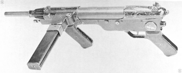 This upper left side view of the Austen MK II has the stock assembly missing. The large disk just above the rear pistol grip would be the pivot point for the folding stock. The notched lug extending out from the receiver, just below the barrel, is the bayonet catch. It can be seen in this picture how the receiver of the Austen Mk II was made up from aluminum die castings, some of the parts being held together with screws as seen just above and in front of the trigger. PHOTO CREDIT: US Army