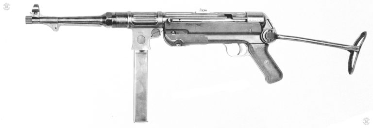 A left side view of the MP38 with the stock extended and a 32-round magazine locked into place. The magazine is of the first style made for the series and has flat, smooth sides with no rimming. The machined ribbing which helped both lighten and strengthen the receiver are plainly seen in this view. The lightening hold in the center of the magazine well is also distinctive to this model weapon. Underneath the barrel, behind the front lug, is the alloy resting bar. The knurled button below the front handgrip is the takedown lock. Pulling the button down and rotating it a half-turn unlocks the upper receiver from the lower, allowing the weapon to be field stripped. Distinctive on the MP38 is the forward-curved cocking lever, seen just behind the magazine housing. The lever is in the forward, uncocked, position. It is this lever, as well as the bolt, telescoping recoil spring assembly, and magazine, that were Hugo Schmeisser patented designs. They led to the MP38-MP40 family of submachineguns to being referred to as “Schmeissers” by Allied personnel. In spite of Schmeisser having nothing directly to do with the weapon’s design. PHOTO CREDIT: US Army