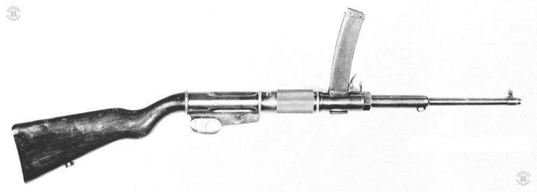 This is a very simple conversion of the Villar Perosa Model 1915 into an individual weapon. The rear of the original design was modified so that a wooden stock could be added. Modifications to the trigger mechanism gave it two triggers, the rear one for full automatic fire, the forward trigger for semiautomatic fire. The safety switch is the rotating lever pm the flat part of the trigger mechanism. The cocking levers of the original design were removed and replaced with a knurled sleeve around the receiver. PHOTO CREDIT: US Army