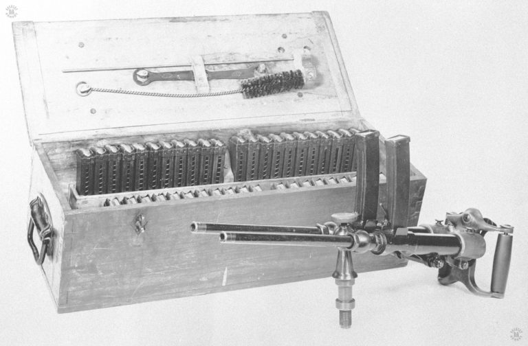 The standard Villar Perosa twin gun on a central pedestal mount. The large case is the transport box for both the Villar Perosa as well as its ammunition and maintenance materials. In each of the two rows on the side of the case are 22 of the 44 magazines that were issued with the weapon. An assistant gunner would carry the case when the weapon was being employed and supply the gunner with reloads. Each magazine held 25 rounds. It can be seen by this photograph, that the Villar Perosa was intended to be employed as a very light crew served machinegun in combat. It is the pistol caliber and automatic fire capability that makes it arguably the first submachinegun, though it took some modifications to properly fit the design into that role. PHOTO CREDIT: US Army