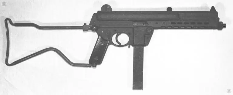 Right side view of the Walther MPL submachinegun. The stock is unfolded and locked in the open position. The safety selector switch is just above the pistol grip where it can be easily reached with the thumb. The switch is set on the bottom “D” position for full automatic fire. Pushed all the way forward to where it points at the trigger would be the “E” setting for semiautomatic fire. The shape of the Walther MP is dictated in part because of the bolt. The  bolt is in the shape of an inverted “L” with the long portion going over the top of the barrel while the breech is near the center of the weapon. PHOTO CREDIT: Kevin Dockery