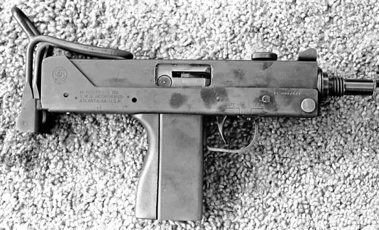 Designed by the SWD Corporation who purchased the rights to the Ingram Model 11 submachinegun design and the Cobray logo in 1982. In 1983, the SWD Corporation released their new submachinegun, the M11/Nine onto the market. The name indicates that the weapon is chambered for the 9x19mm round, but is generally the same size as the original Ingram M11 but with a longer receiver. This illustration is the right side of an unloaded M11/Nine with the stock in the folded position. The stock has been changed so that it is more comfortable and secure to shoulder. It is also easier to employ as it can be grasped with a finger though the buttstock loop and the stock extended to stop when engaged by the stock catch. The cocking knob at the top of the receiver is flat and has no sighting groove down its center. The cocking knob also cannot be rotated to lock the bolt in position. The safety is the same sliding model as found on the Ingram submachineguns on the right side of the trigger guard. This specimen has its safety set in the “FIRE” position. PHOTO CREDIT: Kevin Dockery