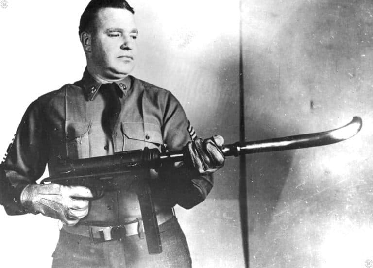 A US Army Master Sergeant holding an M3 submachinegun attached to the 90-degree curved barrel attachment. This photo is circa 1953 during the Korean War. Though the device is not to heavy to hold, the operator is wearing thick leather gloves. These are necessary due to the heat that will be generated in the attachment when it is fired. The heat being a combination of that generated by firing the weapon and the friction of the bullet passing through the curved portion of the barrel. The photo does demonstrate that the curved barrel attachment can be used to shoot around corners without exposing the firer, but it is not a very practical matter. PHOTO CREDIT: US Army