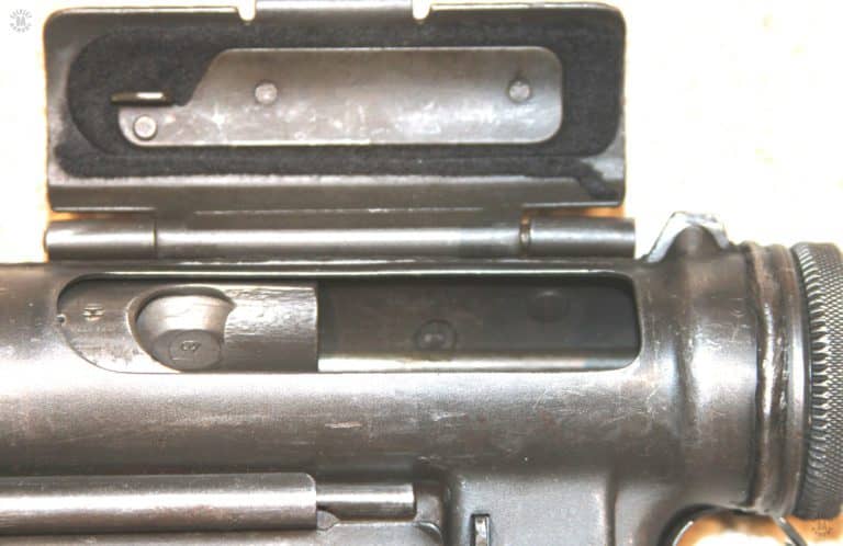 The open ejection port of the M3A1 submachinegun with the bolt in the fully cocked position. The ejection port cover is open so the weapon could be fired from this condition. The safety lug on the bottom of the ejection port cover would engage the front (cocking) hole of the bolt if it was closed. The small projection in front of the ejection port hinge to the left in this illustration is the blade of the front sight. PHOTO CREDIT: Kevin Dockery
