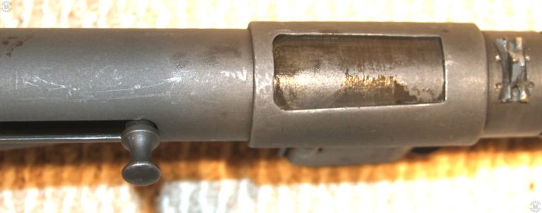 A look down at the top of a Mk II Sten receiver. The magazine housing has been rotated to the down position and this illustration shows how the ejection port is completely closed off from the inside of the receiver. The Mk 5 safety cocking handle at the front of the handle slot, is pressed in to lock the bolt in position. The Mk 5 safety cocking handle is recognizable from this side by the mushroom head above the inwardly curved body of the part. This makes the cocking handle easier to pull out from the locked position and prepare the weapon for firing. The front sight at the far right in the picture has been inserted into its dovetail and secured in place by the punch marks on either end of the dovetail. PHOTO CREDIT: KEVIN DOCKERY