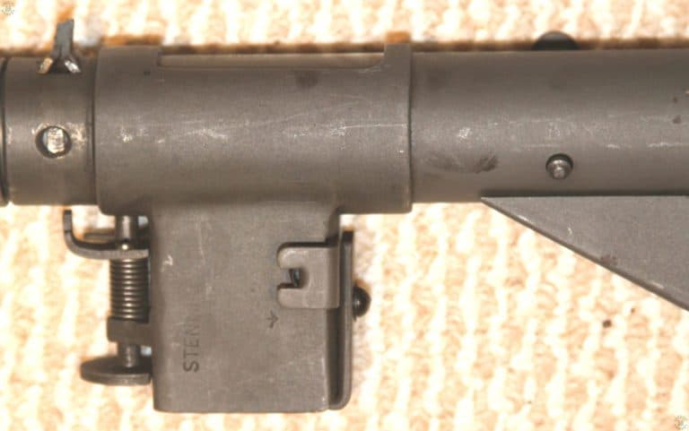 A Sten Mark II submachinegun with the Mk 2 magazine housing unlocked and rotated downwards into the travelling position. A magazine cannot be locked in place when the housing is pointed downwards. The main intent of the rotating magazine housing is to allow the operator to reduced the width of the weapon by nearly half. This makes it much easier to be packed for transport by container or use by a parachutist. This specimen has also been fitted with the Mk 5 safety cocking handle, the base pin of which is protruding through the hole drilled for the purpose in the lower side of the receiver housing. PHOTO CREDIT: KEVIN DOCKERY