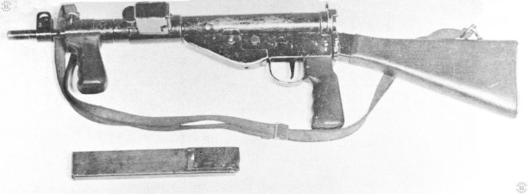 The left side of a Mk V Sten. This specimen is complete with the sling and forward vertical handgrip. A standard 32 round magazine is laying across the bottom of the photograph. PHOTO CREDIT: US ARMY