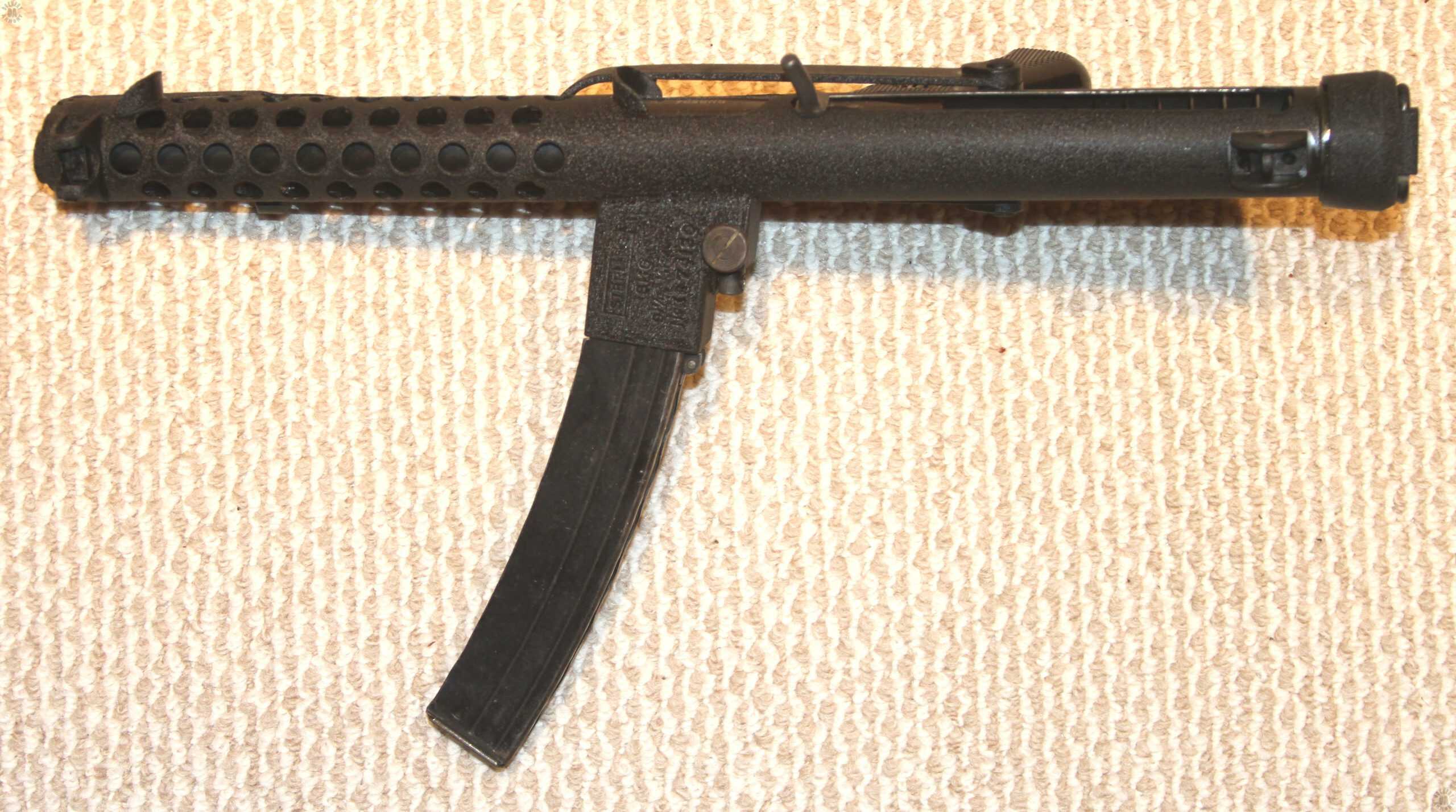 A top-view of a Sterling Mk 4 intended for commercial sale. The stock has been folded and secured underneath the weapon. On the right (upper) side of the weapon the bolt is in the forward (uncocked) position. In front of the ejection port, just ahead of the cocking lever, is the fixed guard intended to keep and operator’s fingers from slipping back into the ejection port while firing. The curved magazine is very distinctive in this picture. PHOTO CREDIT: KEVIN DOCKERY