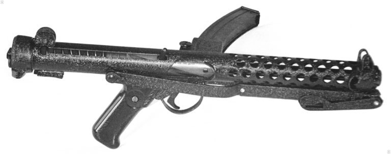 The right side of a Mk 4 Sterling with the stock folded. The upper portion of the stock that is folded up underneath the barrel casing is locked into one of the cooling ports. Pulling down on the butt plate releases the butt catch from the cooling port and allows the stock to be unfolded. The bolt is in the forward (uncocked) position. The crackle-paint finish gives the outside of this weapons a sparkling appearance under photo lights. PHOTO CREDIT: KEVIN DOCKERY