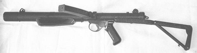 The left side of a Sterling Mk 5. The large front grip is the main identifying point between the Mk 5, made for international commercial sales, and the L34A1 which has no such front block. The Mk 5 is also most often seen with the crackle-finish paint as compared to the smooth matt finish on the L34A1. Other than those characteristics, the two weapons are effectively identical. One feature only found on the commercial Mk 5 weapon is the mounting studs for the Sterling sight rail. The rear stud can be seen on the top of the receiver just in front of the rear sight. This specimen is set on semiautomatic fire according to the position of the selector switch behind the trigger. PHOTO CREDIT: KEVIN DOCKERY