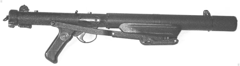 The right side of a Sterling Mk 5 with the stock folded. This commercial weapon has the front handgrip mounted underneath the barrel by a clamping strap around the body of the suppressor. A recess cut into the underside of the front grip accepts the front of the folded stock. The folded stock is secured in place by attaching to a stud inside the cutout underneath the front grip. The two studs use to mount the Sterling sight rail are visible on the top of the receiver, in front of the rear sight and above the center of the ejection port. PHOTO CREDIT: KEVIN DOCKERY