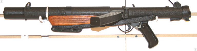 The commercial Mk 5 submachinegun in tended for international sales. This weapon has the crackle finish often seen on this model of Sterling. The stock is folded and locked in place under the wooden front grip. The ring strap used to secure the front grip is the smooth metal above the grip. Ahead of the ring is the front sling mount attached to the side of the suppressor body. The two studs used to mount the Sterling sight rail are on top of the receiver, just in front of the rear sight and above the rear portion of the magazine well. The central threaded hole on the studs can also be seen. PHOTO CREDIT: KEVIN DOCKERY