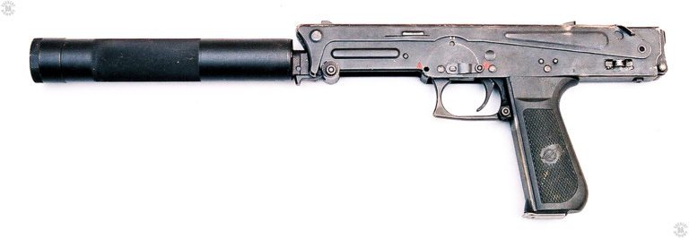 The left side of the PP-93 submachinegun with the suppressor attached. The stock is folded down along the top of the receiver. The small curved shoulder piece of the stock is down along the front of the receiver. Just behind the shoulder piece, underneath the receiver, is the serrated end of the cocking piece for the weapon. The small dot in the center of the circle among the serrations is the lock for the cocking piece. The piece would be grasped and pulled back to just in front of the trigger guard to cock the weapon. The slightly rounded front edge of the trigger guard is to allow for a more secure two-handed hold on the weapon. Above the center of the trigger guard is the safety/selector switch. The switch is rotated so that it is pointing to the rear, the setting for semiautomatic. With the switch pointing straight up, the weapon is on safe and the bolt is locked in place. With the switch rotated to the forward position, the weapon is set on full automatic. The small loop welded on to the side of the receiver, below the back of the stock, is for the attachment of a sling. The small button on the bottom side of the end of the receiver is the lock for the extended stock. The button at the bottom rear of the trigger guard is the pistol-style magazine catch. The weapon is loaded with the 20-round magazine, which sits flush with the bottom of the pistol grip. PHOTO CREDIT: DUTCH HILLENBURG