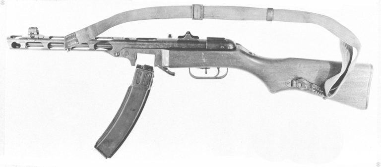 Left side of a PPSh-41 with the 35-round box magazine removed. The magazine catch is partially folded back out of the way. On top of the receiver above the magazine well, is the ejection port with the bolt in the forward position. Behind the ejection port is the simple folding leaf sight with protective wings. PHOTO CREDIT: US ARMY