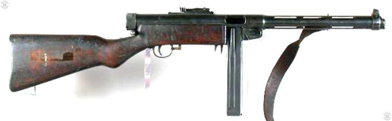 A left-side view of a Suomi Model 1931 with the bolt cocked. The “L” shaped safety/selector switch at the front of the trigger guard is moved fully forward and set in the full automatic fire position. This specimen is loaded with a 50-round “Coffin” box magazine. The quadruple-column stack of ammunition in the magazine gave it a very wide body and an unusual set of followers inside of the magazine. The followers had extended side pieces that helped lift the cartridge stacks as the weapon was fired. Near the top of the magazine, the follower side pieces would stop at the top of the groove seen near the top rear on the side of the magazine. The inside portion of the follower would lift the last few round up into place for feeding. PHOTO CREDIT: Springfield Armory National Historical Site