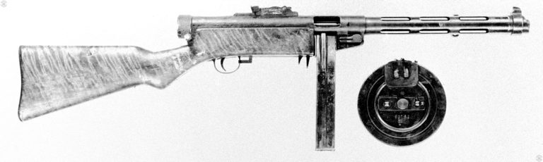 The right side of the Suomi M31 with both the 50-round box magazine (inserted in the weapon) and the 71-round drum to the right in the picture. At the front of the trigger guard is the safety and selector switch. With the switch in the fully forward position, as it is on this specimen, the weapon is set for full automatic fire. With the switch pulled back to the middle position, the weapon will fire on semiautomatic only. Pulling the switch all the way back locks the weapon on safe. When the weapon is placed on safe, the bolt is locked in position whether cocked or uncocked. The barrel jacket locking lever is on the bottom rear of the barrel jacket, just in front of the magazine well. The magazine catch is the longer lever just behind the magazine well. The rear lever is a guard to prevent the magazine catch from being operated accidentally. The cocking lever is the small knob underneath the rear of the receiver. PHOTO CREDIT: US ARMY