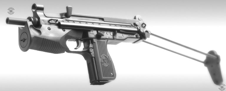 A left-side forward view of the PM-68 submachine gun. The mounting area in the front grip has been filled with the usual threaded screw plug rather than an illuminating device or laser. The weapon has been loaded with the 15-round magazine which sits flush with the bottom of the pistol grip. Just behind and below the trigger is the checkered round magazine catch underneath the small curved guard that protects it from accidental pressing. Above the center of the pistol grip is the bold catch in the down position. This is the position it would be pressed down into to release the bolt when it is held back by the catch.
     The selector switch behind and above the pistol grip is in the fully up position indicating that the weapon is on safe and the bolt is locked in place. The stock has been fully extended and pivoted down at an angle when it is locked in place. The downward angle of the stock allows the butt plate to be secured against the shoulder while raising up the line of sight so that careful aiming can be done with the iron sights. The cocking knob is the long, ambidextrous version that can be operated with either hand. It is the tall, wide position of the cocking handle that has given this weapon the nickname Ucho [the Ear] among Polish troops. PHOTO CREDIT: FABRYKA BRONI