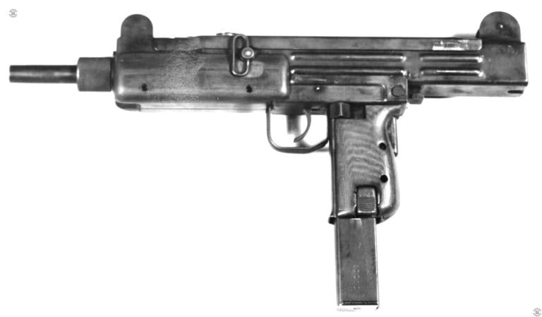 A left-side view of one of the first five pre-production Uzi submachineguns produced in 1950-1951 with the wooden stock removed. The weapon is loaded with the then-standard 30 round magazine. This style of magazine was soon replaced with a 32-round magazine. As can be more clearly seen in this photo, the safety/selector switch markings are not on this very early specimen. The barrel nut is slightly different from the later production version with shallow knurling. The barrel nut latch above the nut and in front of the receiver is also smaller than that of the production weapon. In spite of not having the stock attached, the Uzi in this configuration was still considered easy to handle and could be fired with only one hand if necessary. PHOTO CREDIT: US NAVY HISTORICAL ARCHIVES