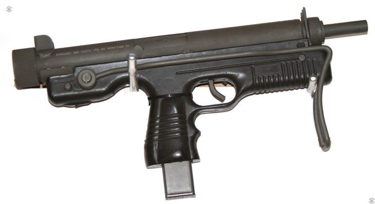 A Kommando carbine with the stock folded. The grip safety is missing on this specimen, the slot where it would normally be mounted can be seen at the bottom and rear of the trigger guard. The simple wire stock would be pulled down and rotated underneath the weapon to extend it. The stock would be braced in place for use by it pressing against the two studs extending out from the receiver. The right-side stud can be seen behind the rear of the stock pivot. The weapon is loaded with a 25-round magazine. PHOTO CREDIT: KEVIN DOCKERY