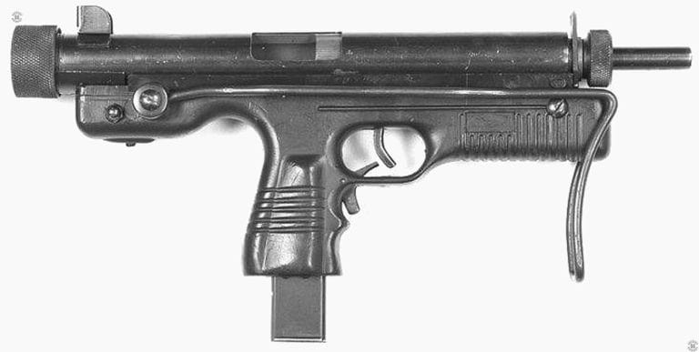 A right-side view of the Kommando carbine with the stock folded. The bolt is open in the cocked position. Below and behind the trigger and trigger guard is the simple L-shaped grip safety.