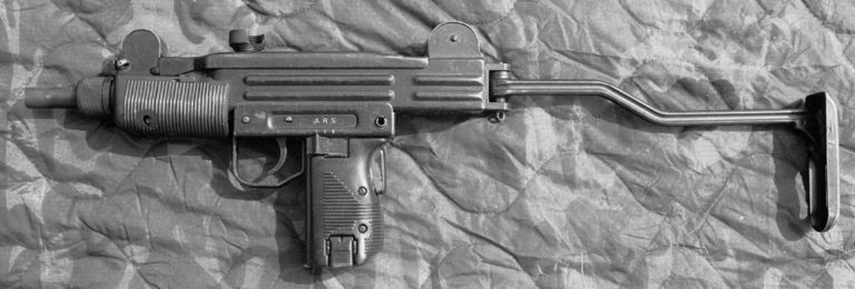 The left side of an unloaded Mini-Uzi with the stock extended to be braced against the shoulder when the weapon is fired. This weapon is a “sterilized” version with no markings on the receiver or parts beyond the serial number of “88.” The markings for the selector switch, at the top of the pistol grip, are A, R, and S, for Automatic, Repeat (Semiautomatic), and Safe. The sliding selector switch, directly behind the trigger, is set to the forward, “A” position for full automatic fire. At the bottom of the pistol grip is the magazine catch. PHOTO CREDIT: KEVIN DOCKERY