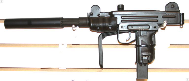 The left side of a suppressed Mini-Uzi. The suppressor is an American commercial product and threads on in place of the barrel nut on the front of the receiver. This specimen is loaded with a 25-round magazine. Markings for the selector switch, at the top of the pistol grip, are A, R, and S, for Automatic, Repeat (Semiautomatic), and Safe. The sliding selector switch, directly behind the trigger, is set to the forward, “A” position for full automatic fire. At the bottom of the pistol grip is the magazine catch. PHOTO CREDIT: KEVIN DOCKERY