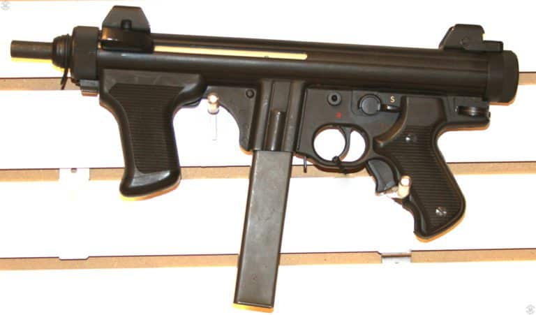 Right side of the Beretta PM12S with the unseen stock folded to the left side. The pivot point for the stock is the disk seen at the rear of the lower receiver, behind the pistol grip. The safety/selector switch is above and behind the trigger, where it can be rotated by the right thumb of the shooter. The white “S” is for safe, the red “1” for semiautomatic fire, and the red “R” for Raffica – full automatic fire. Below and behind the trigger guard, on the rear pistol grip. Is the grip safety that would be held in by the shooters fingers. The central magazine keeps the weapon balanced even as the ammunition is fired. PHOTO CREDIT: Kevin Dockery
